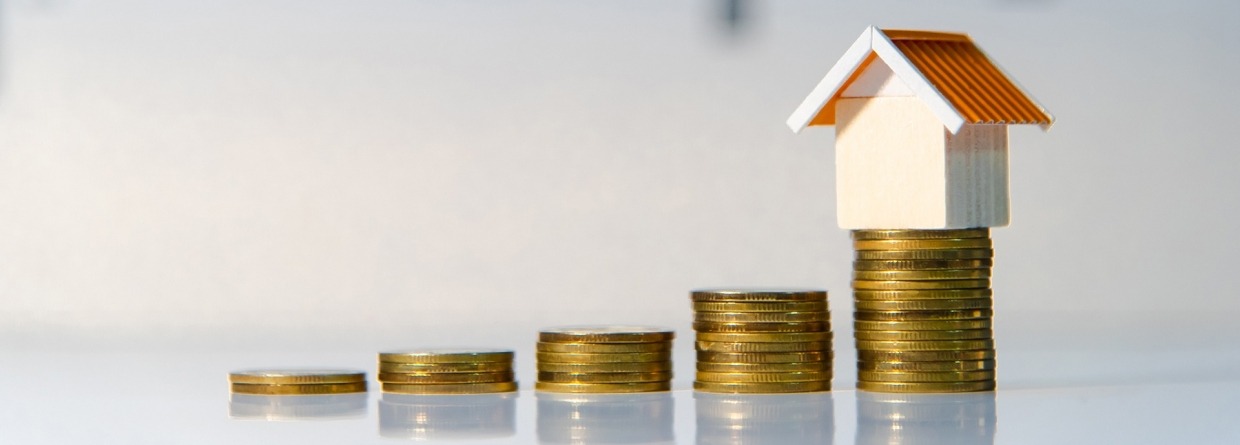 Oplopende stapel met munten geld en op de laatste stapel staat een huis