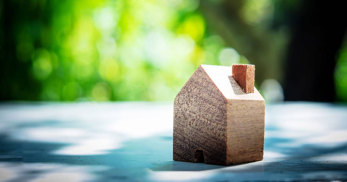 Een houten huisje op een tafel met een achtergrond van bomen en groene bladeren