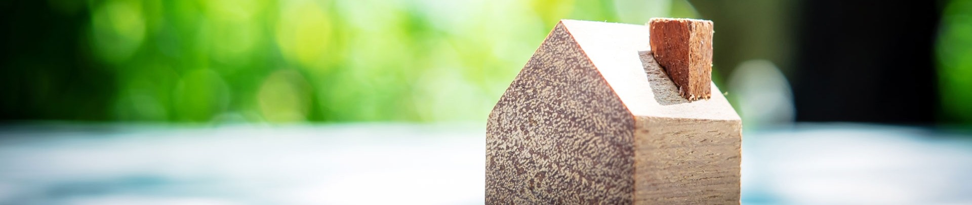 Een houten huisje op een tafel met een achtergrond van bomen en groene bladeren